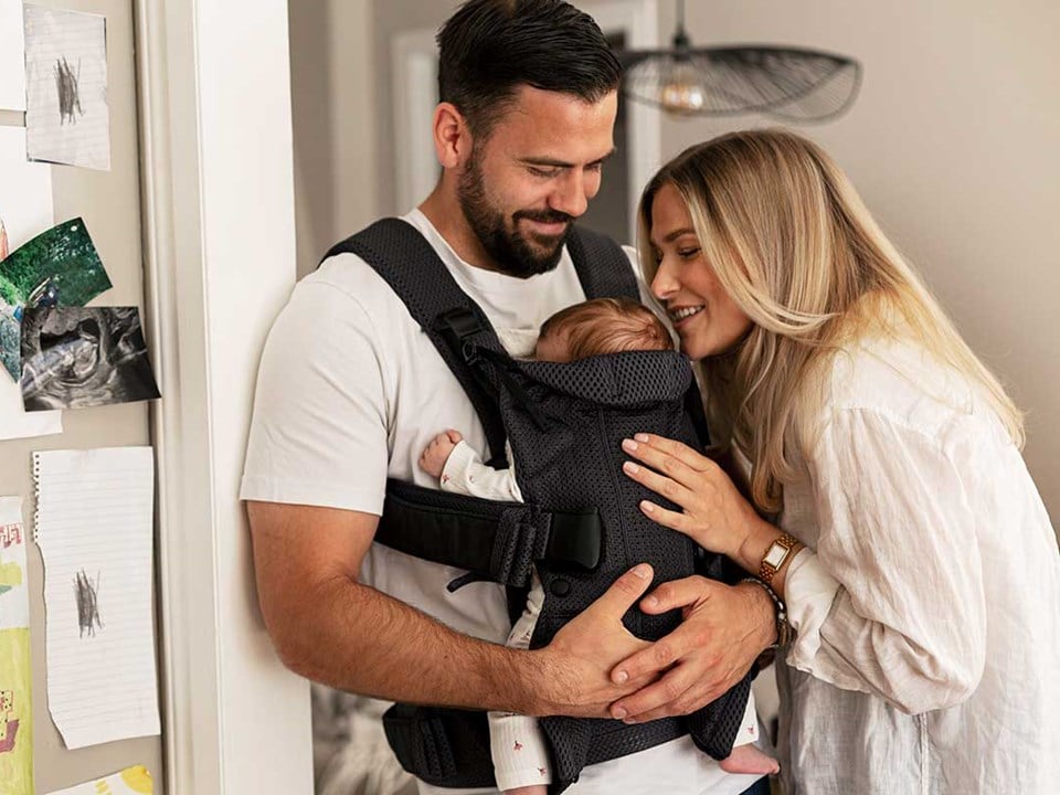 Mor og far med baby i bæresele, til illustrasjon for personlig økonomi