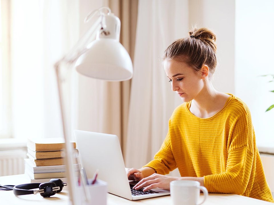 Jente i orange genser med PC, til illustrasjon for ung voksen på vei inn i voksenlivet