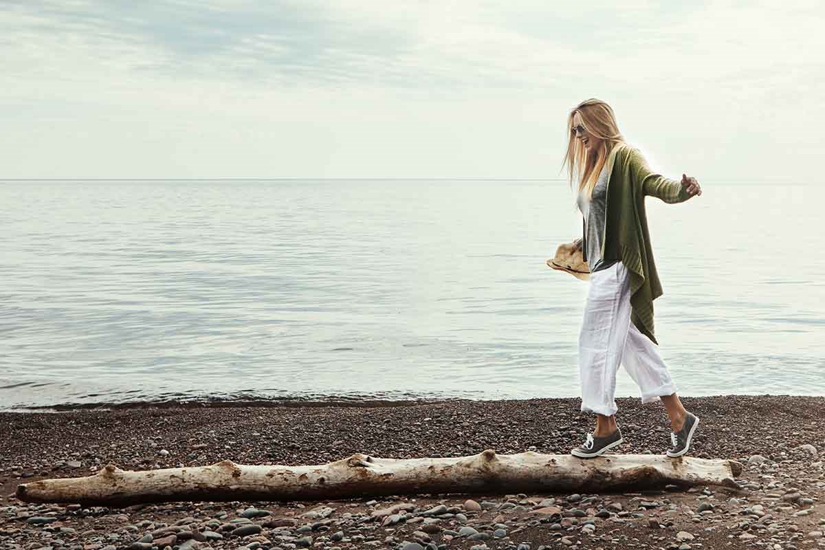 Dame balanserer på stokk ved stranden, til illustrasjon for feriepenger