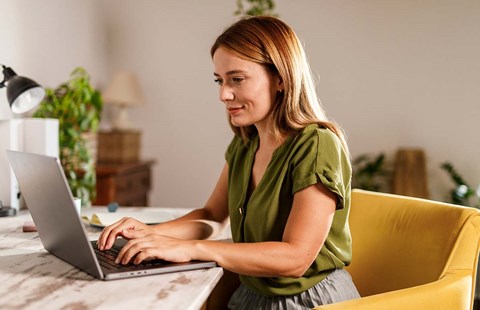 Dame med laptop hjemme i stua, illustrasjon til pensjonssparing