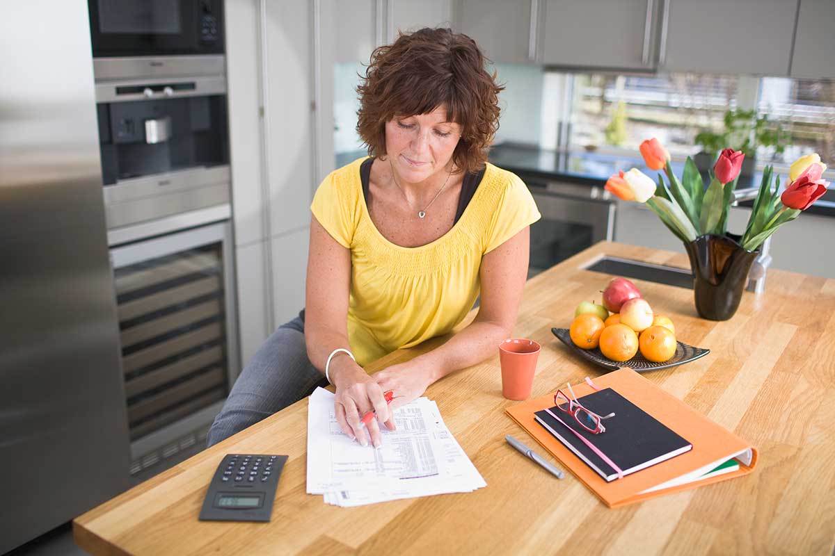Dame ser på papirer ved kjøkkenbordet, til illustrasjon for spareplan