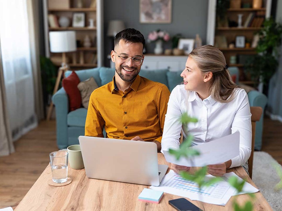 Par sitter ved spisebordet og ser på papirer og pc, til illustrasjon for hvordan spare 100.000 kr