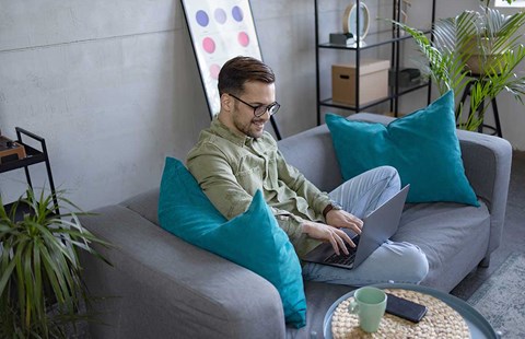 Mann sitter i sofa og jobber på PC, til illustrasjon for hvordan spare penger
