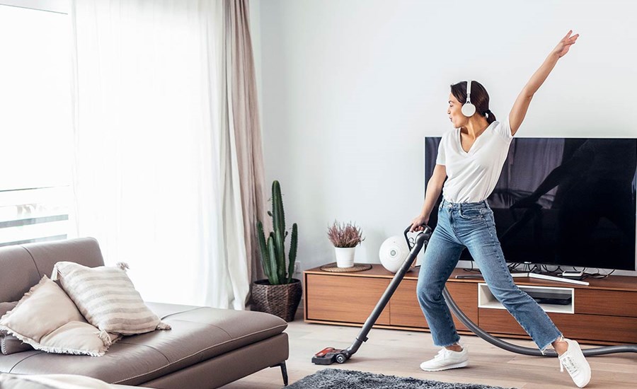 Ung jente danser mens hun hører på musikk og støvsuger boligen, til illustrasjon for BSU