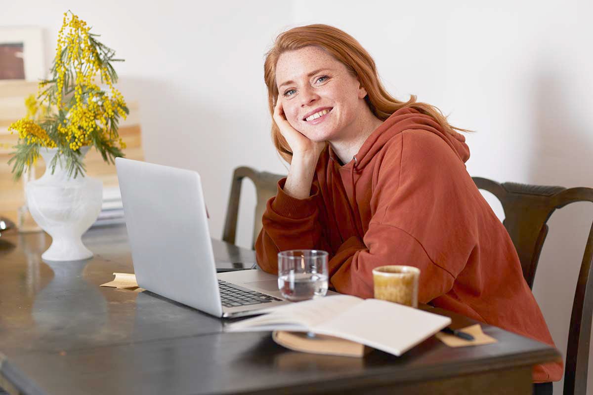 Ung jente sitter på kjøkkenbord med datamaskin fremfor seg og smiler, til illustrasjon for sparekalkulator