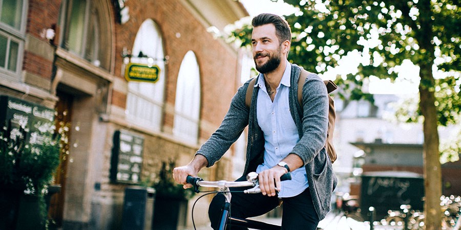 Mann med ryggsekk sykler rundt i sentrum, til illustrasjon for sparekonto
