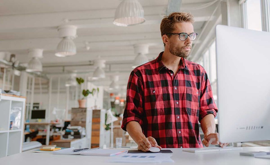 Mann i rutete skjorte ser på mac skjerm, til illustrasjon for bankkort for bedrift