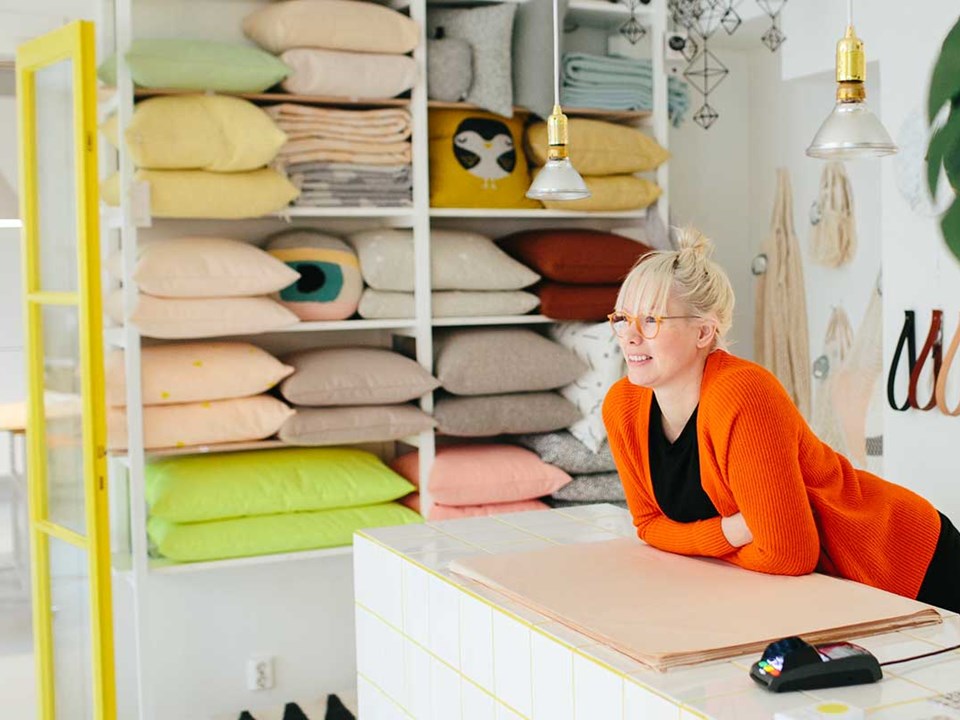 Dame lener seg over disken i interiørbutikken sin med betalingsterminal rett ved