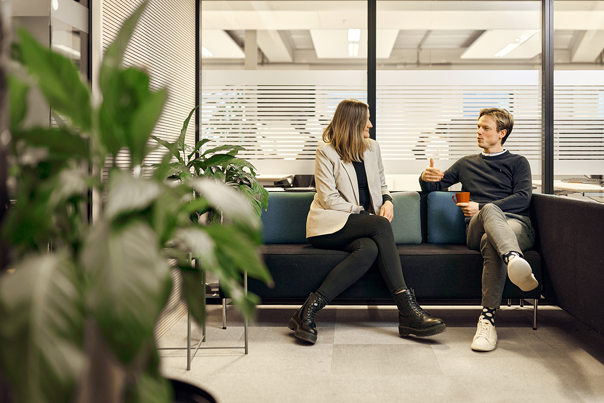To ansatte i BN Bank sitter i en sofa med en kaffekopp og snakker, til illustrasjon for bedriftskunde i BN Bank