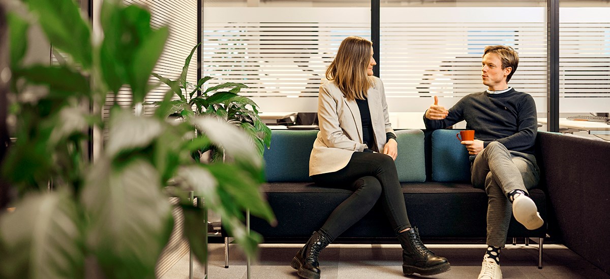 To ansatte i BN Bank sitter i en sofa med en kaffekopp og snakker, til illustrasjon for bedriftskunde i BN Bank