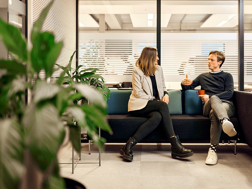 To ansatte i BN Bank sitter i en sofa med en kaffekopp og snakker, til illustrasjon for bedriftskunde i BN Bank