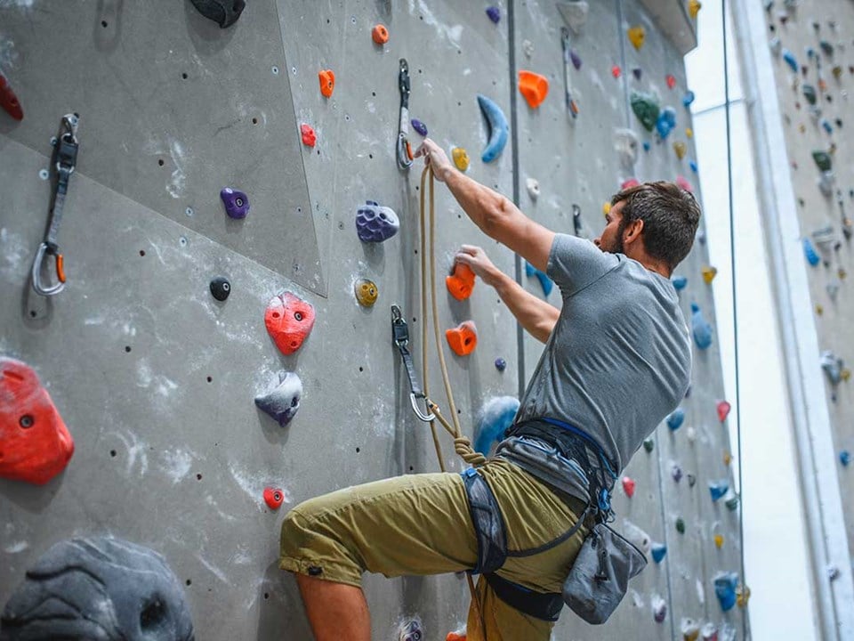 Mann klatrer i klatrevegg, til illustrasjon for bedriftskunder som er i lag og forening
