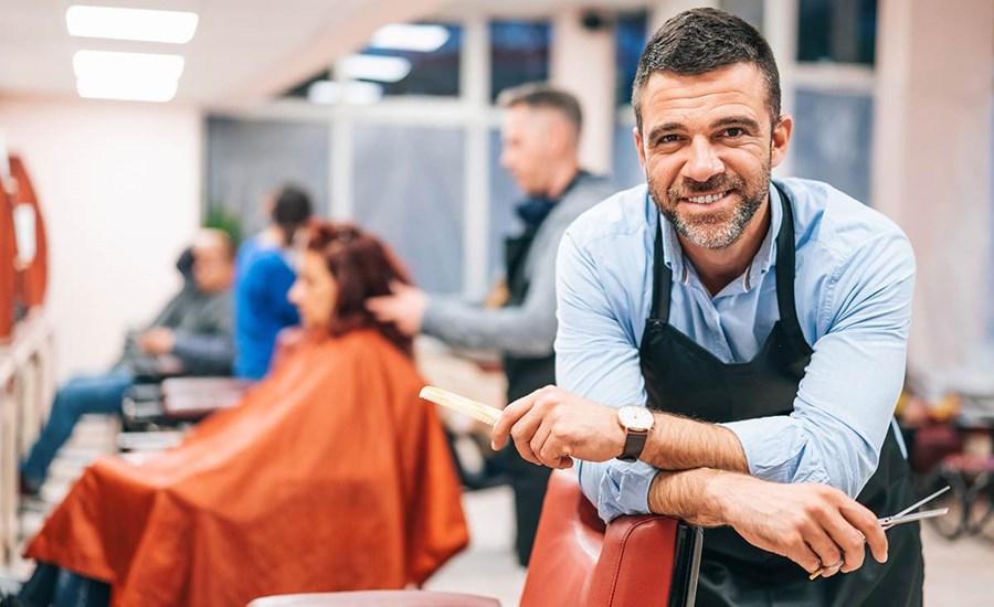 Frisør lener seg over frisørstol i sin egen bedrift, til illustrasjon for driftskonto