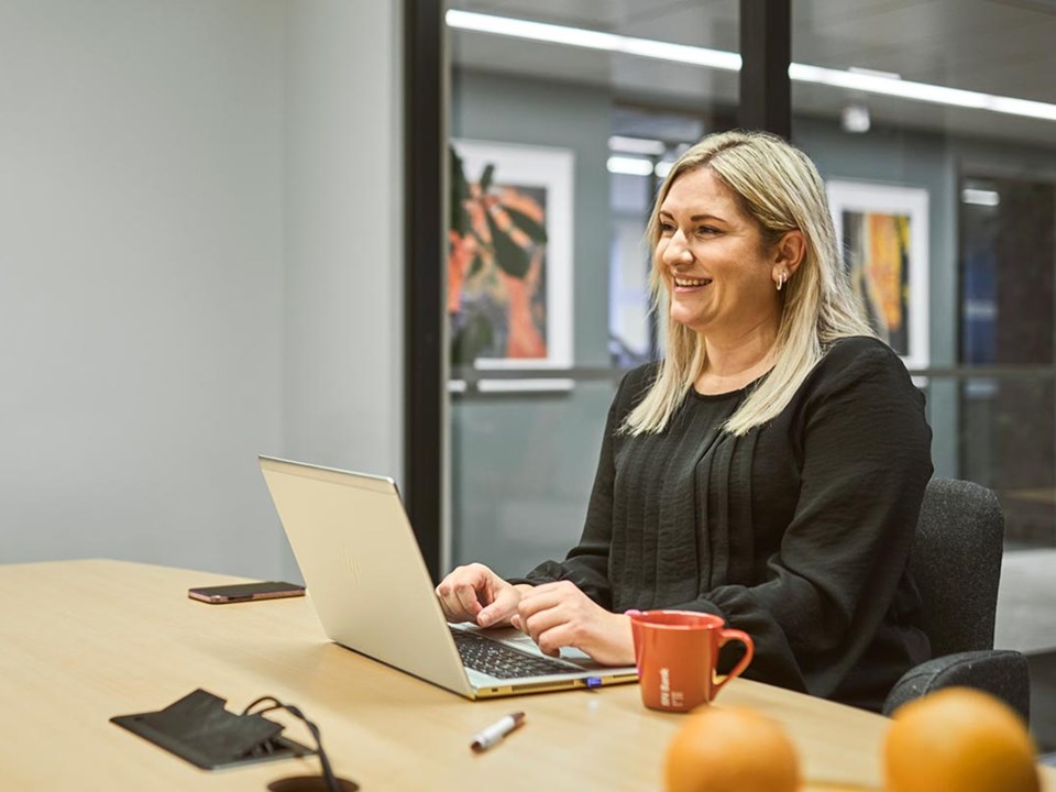 Bedriftsrådgiver Ailin sitter på møterom i BN Bank sine lokaler med en datamaskin fremfor seg, til illustrasjon for bedriftskonto