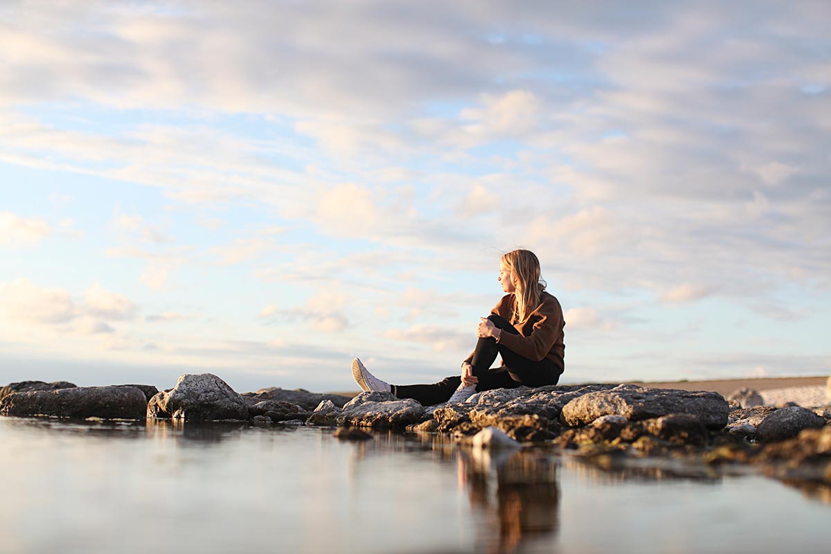 Ung jente sitter på fjærsteinene og ser utover havet, illustrasjon for grønn bank