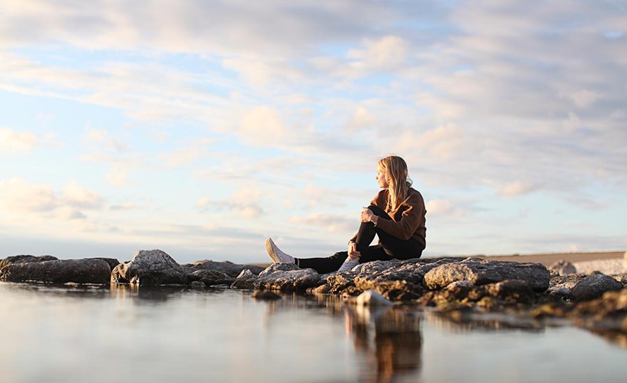 Ung jente sitter på fjærsteinene og ser utover havet, illustrasjon for grønn bank