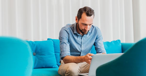 Mann sitter i blå sofa med laptop, til illustrasjon for kredittpolicy