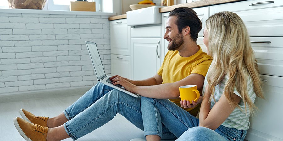 Par sitter på kjøkkengulvet med laptop