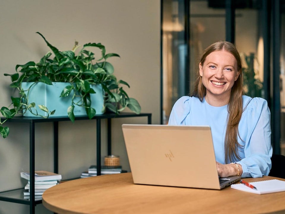 Kvinne sitter foran pc ved et rundt bord