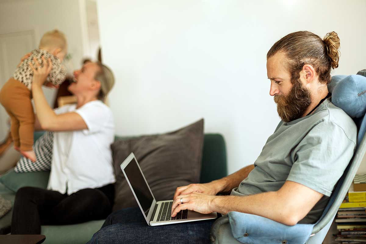 Mann i godstolen jobber på PC med familien i bakgrunnen, illustrasjon til veileder om hvordan endre beløpsgrense nettbank