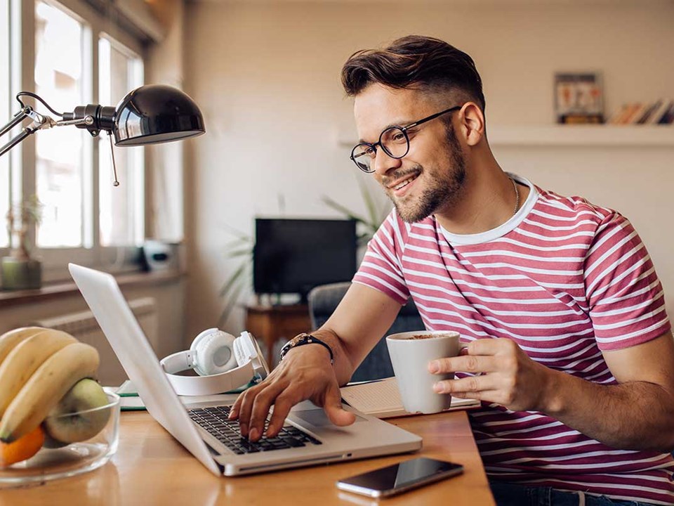 Mann med kaffekopp ser på laptop, illustrasjon til veileder om hvordan legge til betaling i nettbanken