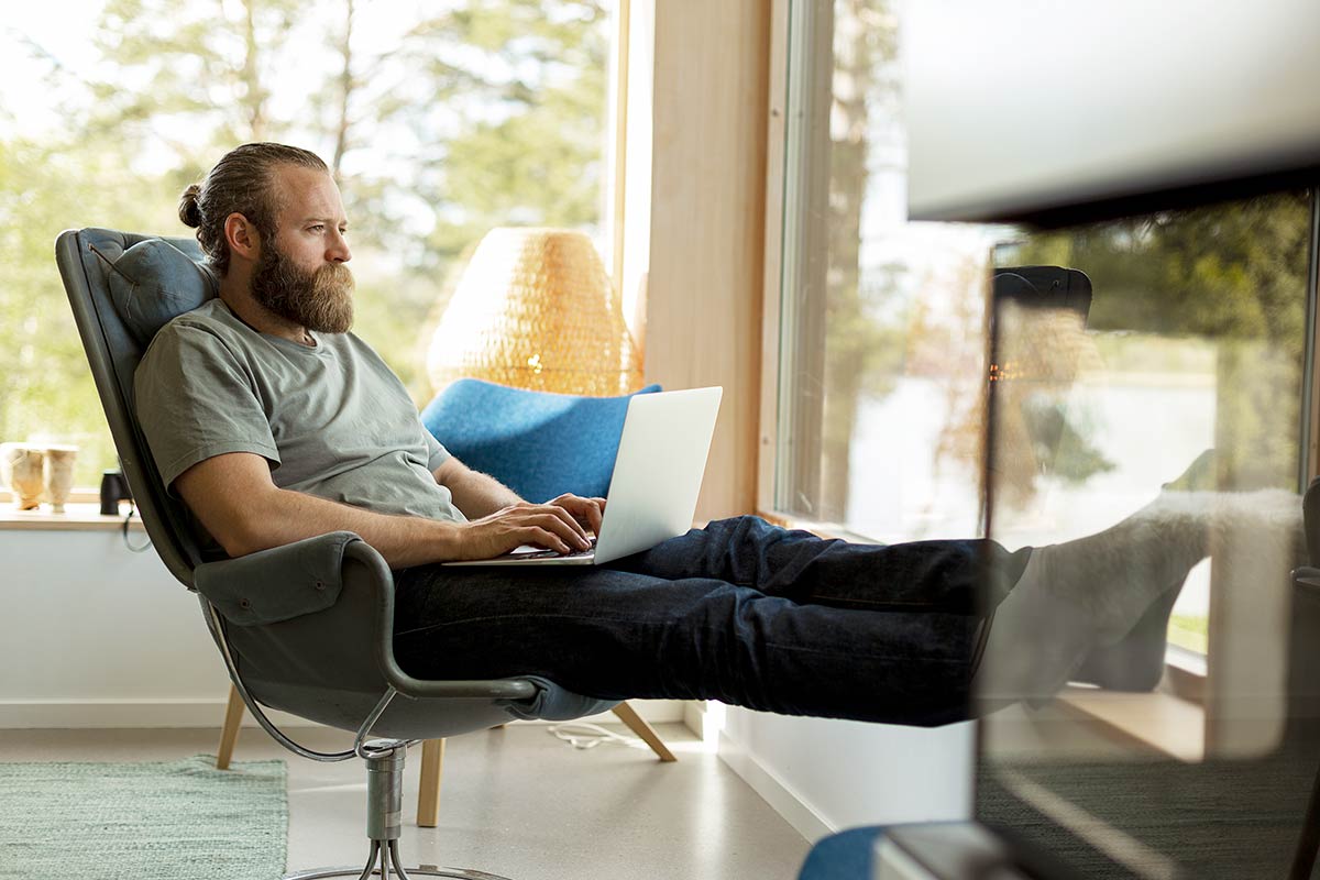Kvinne sitter på sofaen med datamaskin i fanget, til illustrasjon for sikkerhet på nett
