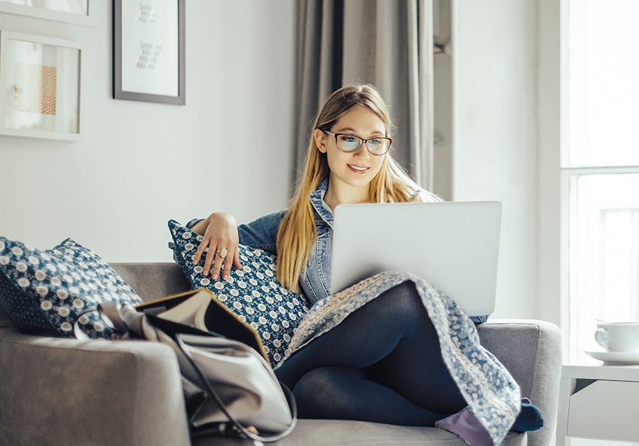 Kvinne sitter på sofaen med datamaskin i fanget