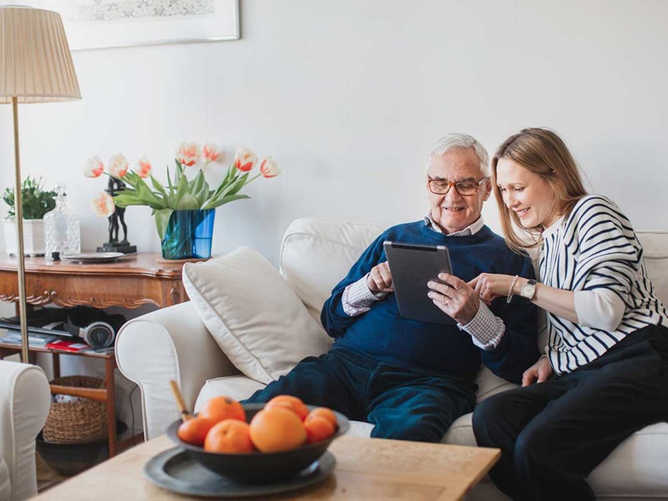 Eldre mann og ung kvinne sitter i en sofa med et nettbrett og skriver fremtidsfullmakt